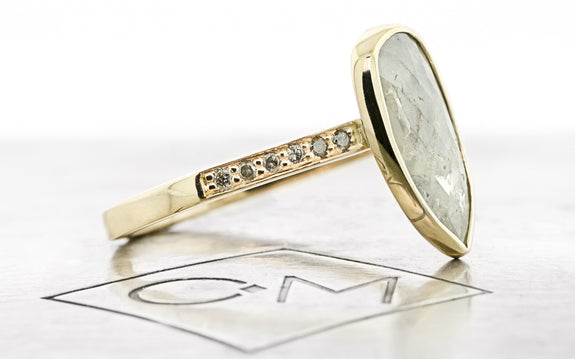 1.41 carat rustic salt and pepper diamond ring bezel set in 14 karat yellow gold with six gray pavé diamonds on each shoulder side view on Chinchar Maloney metal plate