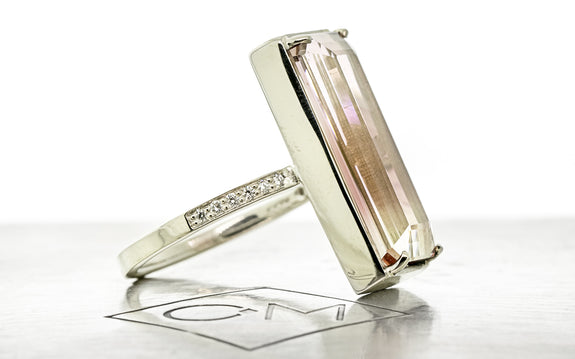 10 carat emerald cut pink tourmaline ring set in 14 karat white gold with six white pavé diamonds on each shoulder side view on Chinchar Maloney metal plate