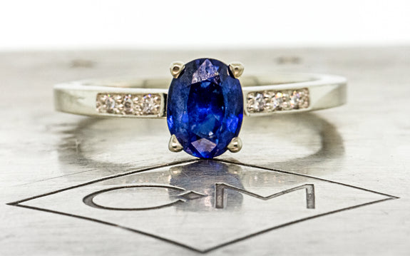 .88 carat blue sapphire with three white pave diamonds on each side front view on Chinchar Maloney metal plate