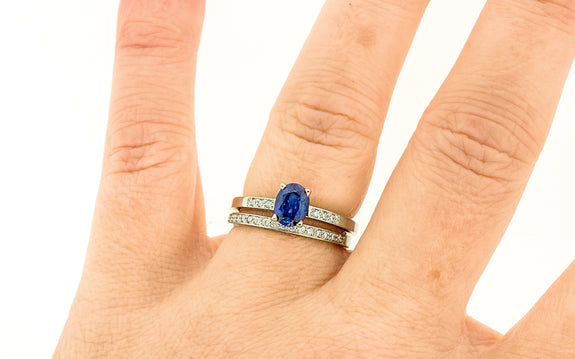 .88 carat blue sapphire with three white pave diamonds on each side paired with 16 white diamond wedding band top view on finger