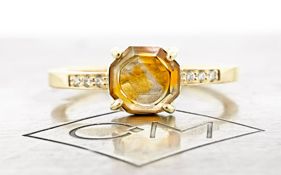 1.31 Carat creamsicle orange Montana sapphire ring in 14 karat yellow gold with three white pavé diamonds on each shoulder front view on Chinchar Maloney metal plate