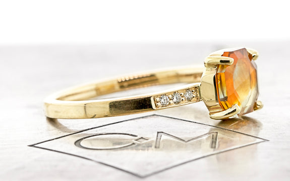 1.31 Carat creamsicle orange Montana sapphire ring in 14 karat yellow gold with three white pavé diamonds on each shoulder side view on Chinchar Maloney metal plate