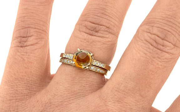 1.31 Carat creamsicle orange Montana sapphire ring in yellow gold with three white pavé diamonds on each shoulder paired with wedding band in 14 karat yellow gold with 16 white pavé diamonds top view on finger