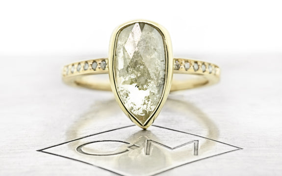 1.41 carat rustic salt and pepper diamond ring bezel set in 14 karat yellow gold with six gray pavé diamonds on each shoulder front view on Chinchar Maloney metal plate